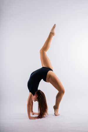 A girl gymnast in a swimsuit does tricks on a white and dark background. Front viewの写真素材