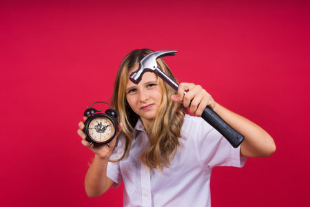Young blonde girl holding alarm clock and hammer smiling and laughing hard out loud.の写真素材