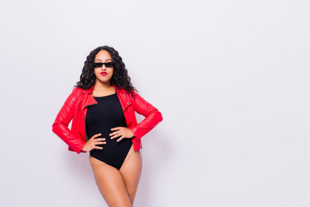 African American curvy female in black bodysuit and jacket on red and white background in studioの写真素材