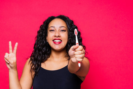 Happy African American woman brushes a teeth. Dental hygiene concept. Isolated on red background.の写真素材