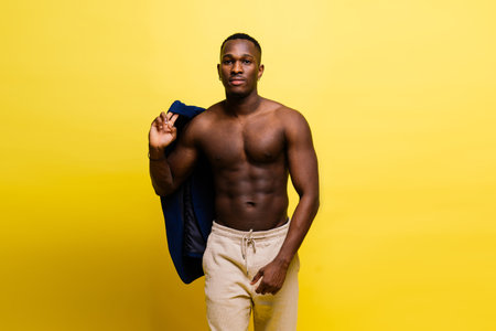 Portrait of an athletic african american man topless smiling, yellow, red and black backgroundの写真素材