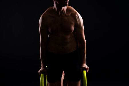 Young muscular man doing parallel bar exercises in dark white red studio with copy spaceの写真素材