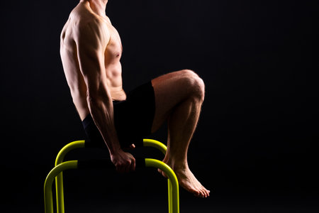 Young muscular man doing parallel bar exercises in dark white red studio with copy spaceの写真素材