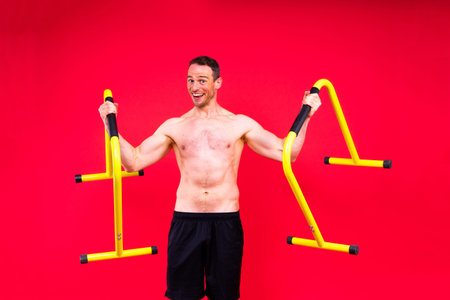 Young muscular man doing parallel bar exercises in dark white red studio with copy space