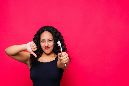 Happy African American woman brushes teeth. Dental hygiene concept. Isolated on red background.の写真素材