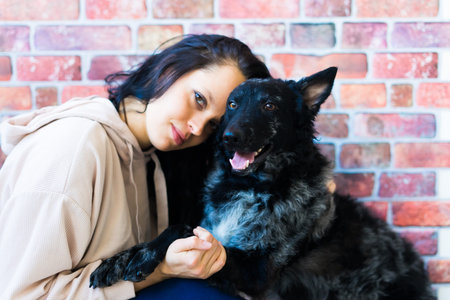 Happy brunette lady in casual wear hugging mudi pet dog, studio background.の写真素材