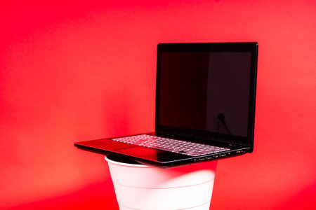 Black laptop in a trash bin on a red background isolatedの写真素材