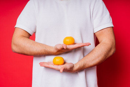Young handsome man with dark hair with tangerine in shirt on red backgroundの写真素材