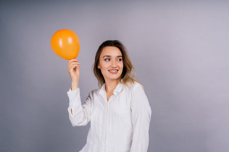 Close up portrait of young woman inflating balloon on isolated grey backgroundの写真素材