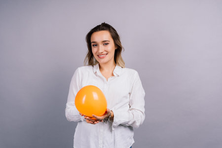 Close up portrait of young woman inflating balloon on isolated grey backgroundの写真素材