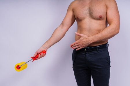 Cheerful young topless man hold paint roller isolated on a grey background studio.の写真素材