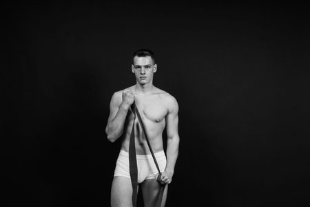 Athlete with a muscular body in white panties is doing physical exercises with rubber