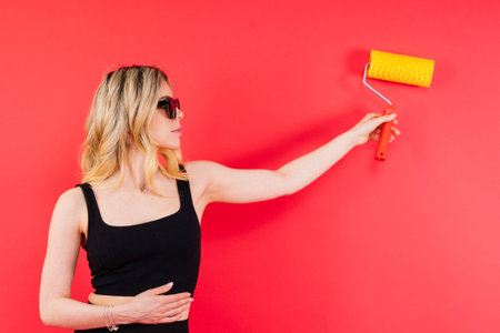 Young woman with roller brush on red white background Instruments accessories for renovation room