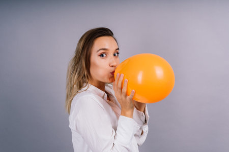 Close up portrait of a young woman inflating balloon on isolated grey backgroundの写真素材