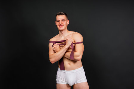 Young bodybuilder working out with rubber band over white and dark background