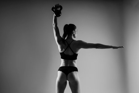 Woman in sportswear doing crossfit workout with kettle bell on a dark yellow red background.の写真素材