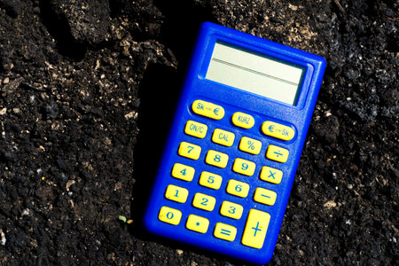 Blue calculator in dark soil, burnt ground after a fireの写真素材