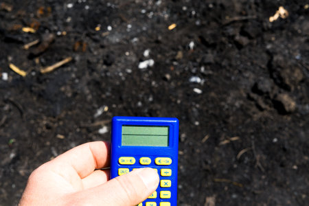 Blue calculator in dark soil, burnt ground after a fireの写真素材