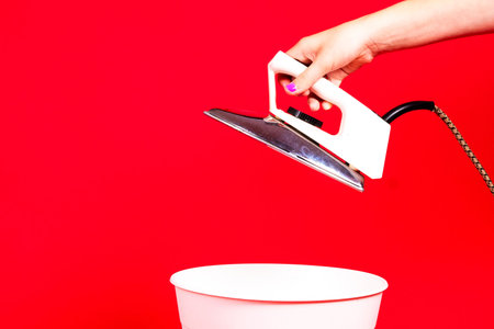 Woman putting iron in recycle bin on red backgroundの写真素材