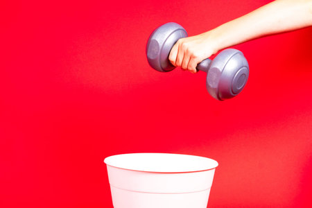 Dumbbells are thrown in the trash can. For copy space for designers on a red background