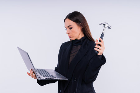 Attractive woman wearing business suit with computer angry facial expression holding hammerの写真素材