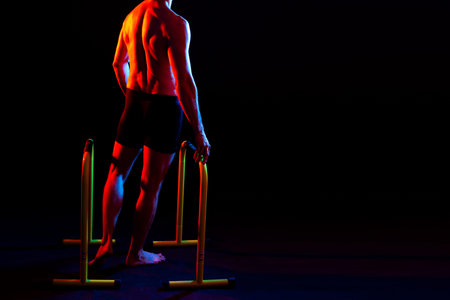 Strong male athlete shows moves on a parallel bars, studio shot