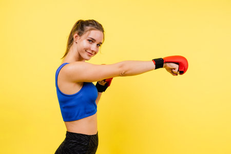 Young woman in a sportswear and boxing gloves standing isolated on yellow background.の写真素材