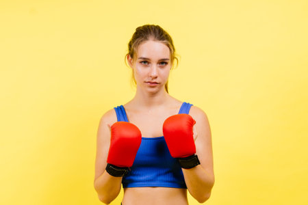 Young tired woman in a sportswear and boxing gloves standing isolated on white yellow background.の写真素材