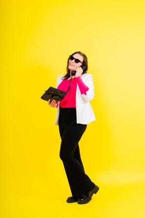 Photo portrait of female holding a phone isolated on yellow backgroundの写真素材