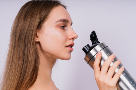 Closeup side view of a sportive female after training who drinking fresh water from sport bottleの写真素材