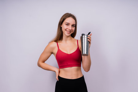 Closeup side view of a sportive female after training who drinking fresh water from sport bottleの写真素材