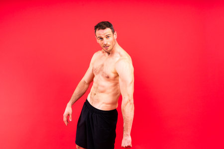 Image of muscle man posing in a studio, dark white red backgroundの写真素材