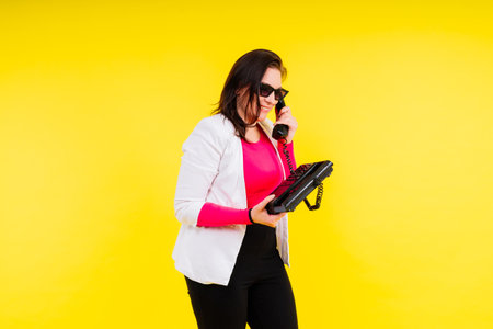 Photo portrait of female holding a phone isolated on yellow backgroundの写真素材