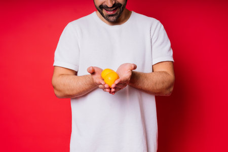 Handsome tall bearded white man with a dark hair with tangerine on red backgroundの写真素材