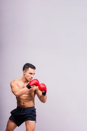 Confident male boxer in red gloves prepares for intense fight in blue studio, showcasing strength and determinationの写真素材