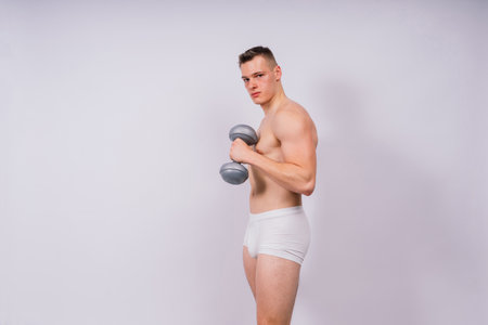 Muscular young man in white underwear with dumbbell in studio backgroundの写真素材