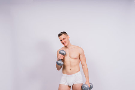 Muscular young man in a white underwear with dumbbell in studio backgroundの写真素材