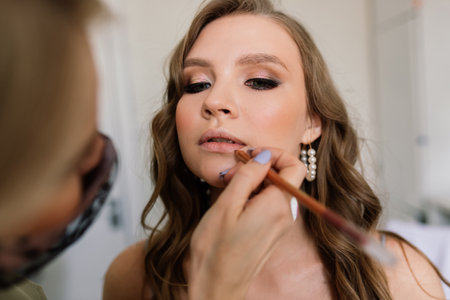 Makeup artist applies lipstick. Hand of make-up master, painting lips of young beauty model.の写真素材