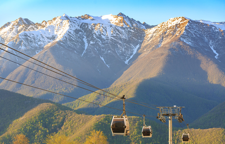 Cabins of funicular on the background of green forests and snow-capped mountains in the spring at sunsetのeditorial素材