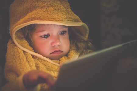 Portrait of a little girl dressed in a nightrobe that sits on the sofa and holds a tablet computerの写真素材