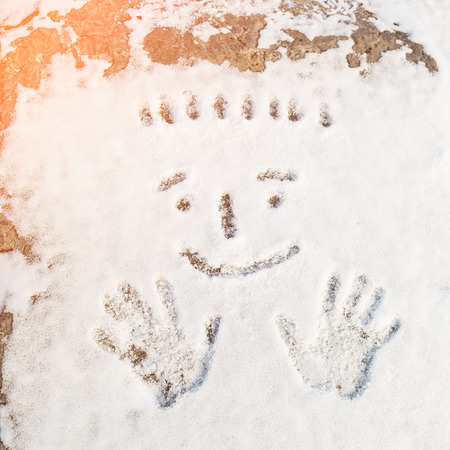 Palmprints of man and a human smiling face drawn on the snowの写真素材