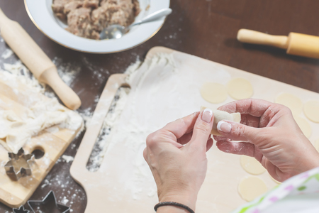 Female hands mold homemade dumplings on the background of a wooden tableの写真素材