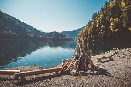 Prepared for kindling a large bonfire and benches from the logs on the shore of a beautiful lake with forest. Toned imageの写真素材