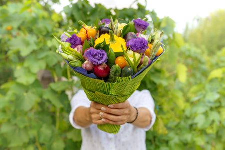 Beautiful bouquet of fresh vegetables and flowers in the hands of a woman as a gift