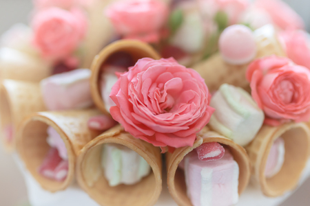 Bouquet of flowers of pink roses, waffle cones, sweets and marshmallows close upの写真素材