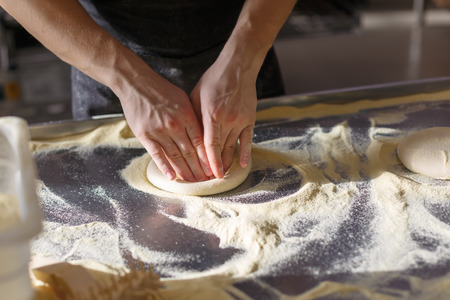 Baker kneads dough for pizza in the kitchen in the restaurantの写真素材