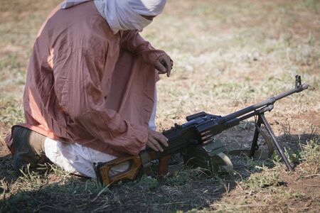 SAMBEK, ROSTOV REGION, RUSSIA, AUGUST 19, 2018: Reconstruction of Afghan war. Muslim dress is sitting on the ground near the machine gunのeditorial素材