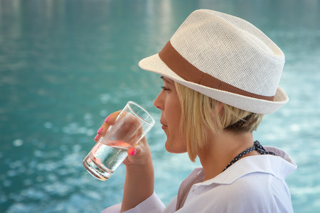 Caucasian blonde girl drinks cold water from a turquoise seaの写真素材