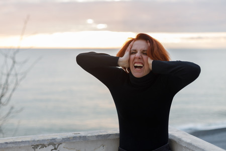 Woman with red hair clutching her headの写真素材