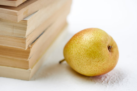Delicious ripe pear near a stack of booksの写真素材